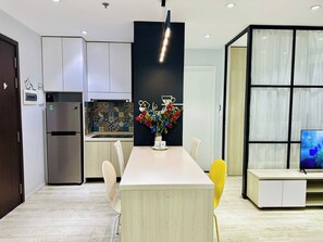 A modern kitchen with white cabinets, a built-in refrigerator, and a dining area with a white table and chairs. - SS Homes River Gate Premium (Ho Chi Minh)