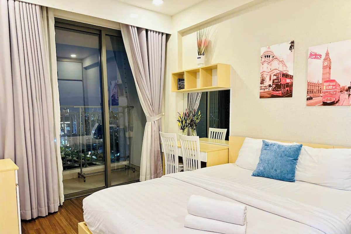 Ein Hotelzimmer mit einem großen Bett, einem Schreibtisch und einem Stuhl, Blick auf die Stadt durch das Fenster und Kunstwerken an der Wand.