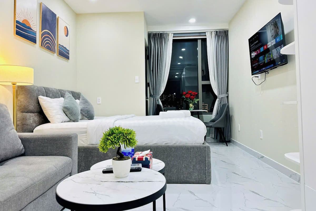 Ein modernes Hotelzimmer mit Bett, Sofa und einem kleinen Tisch mit Pflanze. Vorhänge, ein Fernseher und Kunstwerke sind an den Wänden angebracht.