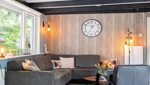 Een moderne woonkamer met een hoekbank, een ronde salontafel en een grote wandklok.