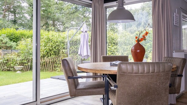 Een eetruimte met een ronde tafel en vier stoelen, een vaas met bloemen en een hanglamp.