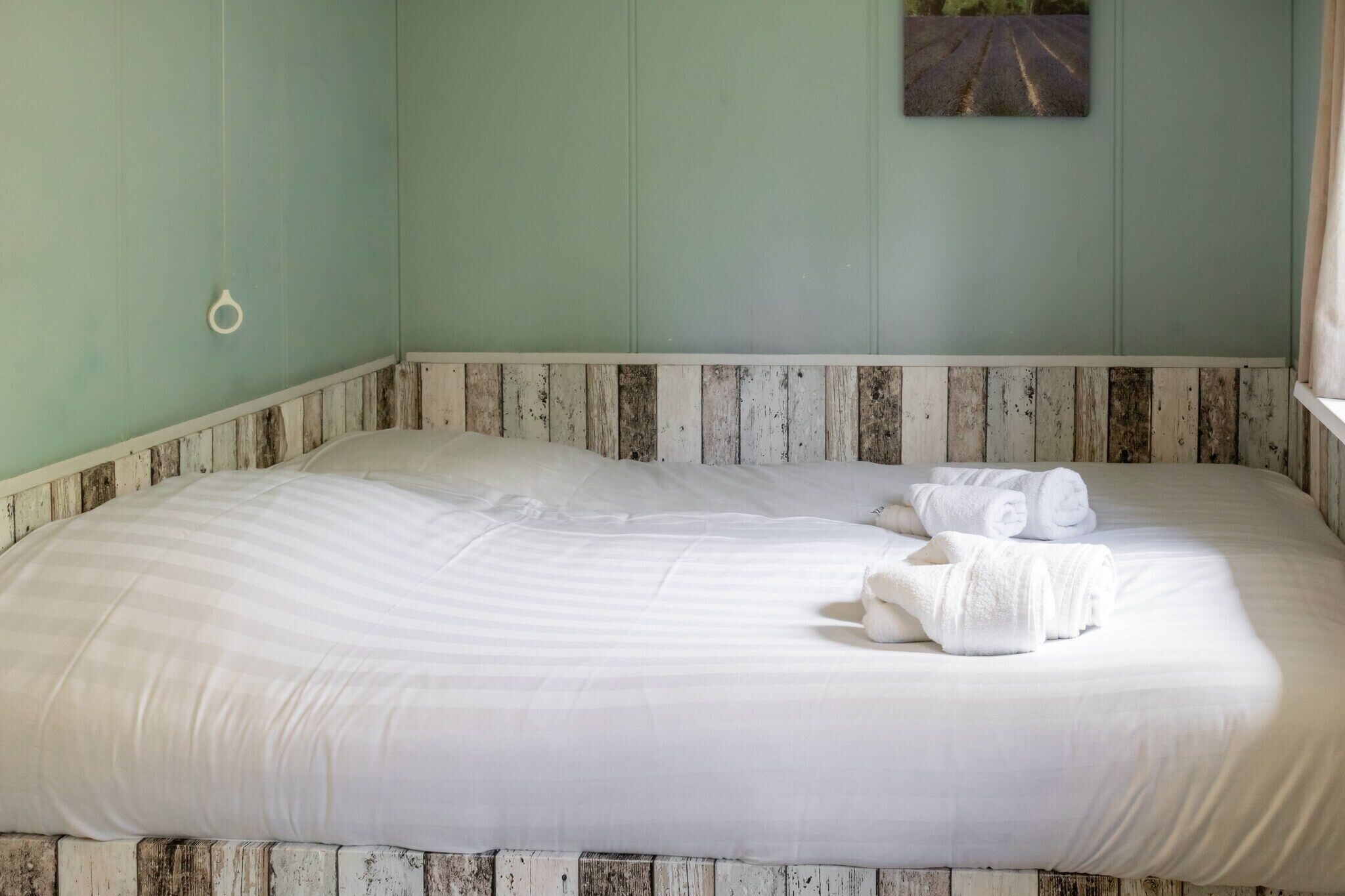 A large bed with white linens, a wooden headboard, and a painting on the wall.