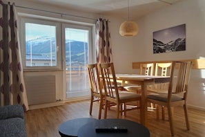 A dining area with a table, chairs, a remote control on a table, and a mountain view through the window.
