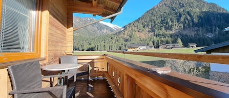 A wooden deck with a table and chairs, overlooking a mountainous landscape.