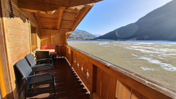A wooden deck with chairs and a table, overlooking a frozen river with mountains in the background. - Apartment in a quiet location with beautiful view (Neukirchen am Großvenediger)
