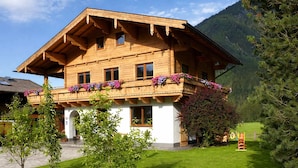 A wooden chalet with a balcony, surrounded by a grassy yard and trees. - Apartment in a quiet location with beautiful view (Neukirchen am Großvenediger)