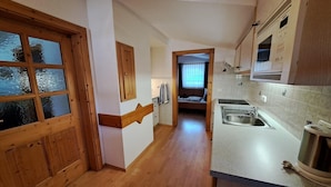 A narrow hallway with wooden flooring, a kitchen area with a sink and countertop, and a bedroom visible through an open door. - Apartment in a quiet location with beautiful view (Neukirchen am Großvenediger)