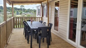 Eine überdachte Terrasse mit Holzdeck, einem Tisch und Stühlen sowie einer Glastür, die zu einem Innenbereich führt.