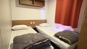 Ein kleines Hotelzimmer mit zwei Einzelbetten, einem Holzkopfende, einer kleinen Ablagefläche und einem roten Vorhang.