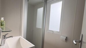 Ein kleines Badezimmer mit weißem Waschbecken, Spiegel, Toilette und Fenster.