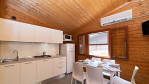 Una cocina compacta con armarios blancos, un microondas, un refrigerador y una zona de comedor con sillas y una mesa blancos.