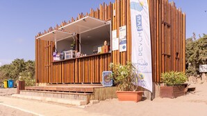 Una estructura de madera con un porche cubierto, posiblemente un quiosco o una pequeña tienda, con un letrero y un banderín en el lado derecho.