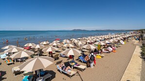 Una playa con muchos sombrillas y tumbonas, una orilla arenosa y el océano al fondo.