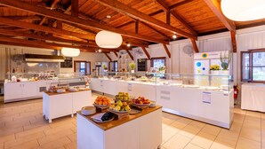 Zona de desayuno tipo buffet con diversos alimentos y una cocina moderna al fondo.