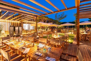 Un espace de restauration en plein air avec des tables et des chaises en bois, des parasols et une structure en forme de pergola.