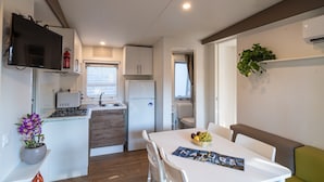 Cocina compacta con estufa, refrigerador y televisor de pantalla plana sobre el mostrador.