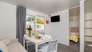 A modern hotel room with a bed, a dining area with a table and chairs, a TV mounted on the wall, and a view of the outside. - Mobile home in Rabac with shared pool (Rabac)