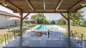 Ein überdachter Außenbereich mit Pool, Liegestühlen, Sonnenschirmen und einem Essbereich.