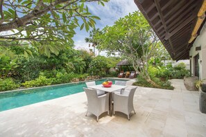 A poolside area with a table and chairs, surrounded by lush greenery and a clear pool. - Peacefully, 3 Bedroom Villa in Seminyak (Seminyak)