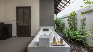 A modern bathroom with a large bathtub, a wooden door, and a small plant area. - Peacefully, 3 Bedroom Villa in Seminyak (Seminyak)