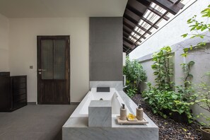 A modern bathroom with a large bathtub, a wooden door, and a small plant area. - Peacefully, 3 Bedroom Villa in Seminyak (Seminyak)