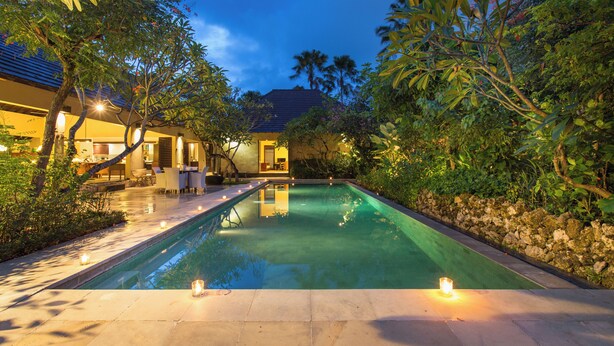 A swimming pool with a stone wall and a patio area with outdoor furniture. - Peacefully, 3 Bedroom Villa in Seminyak (Seminyak)