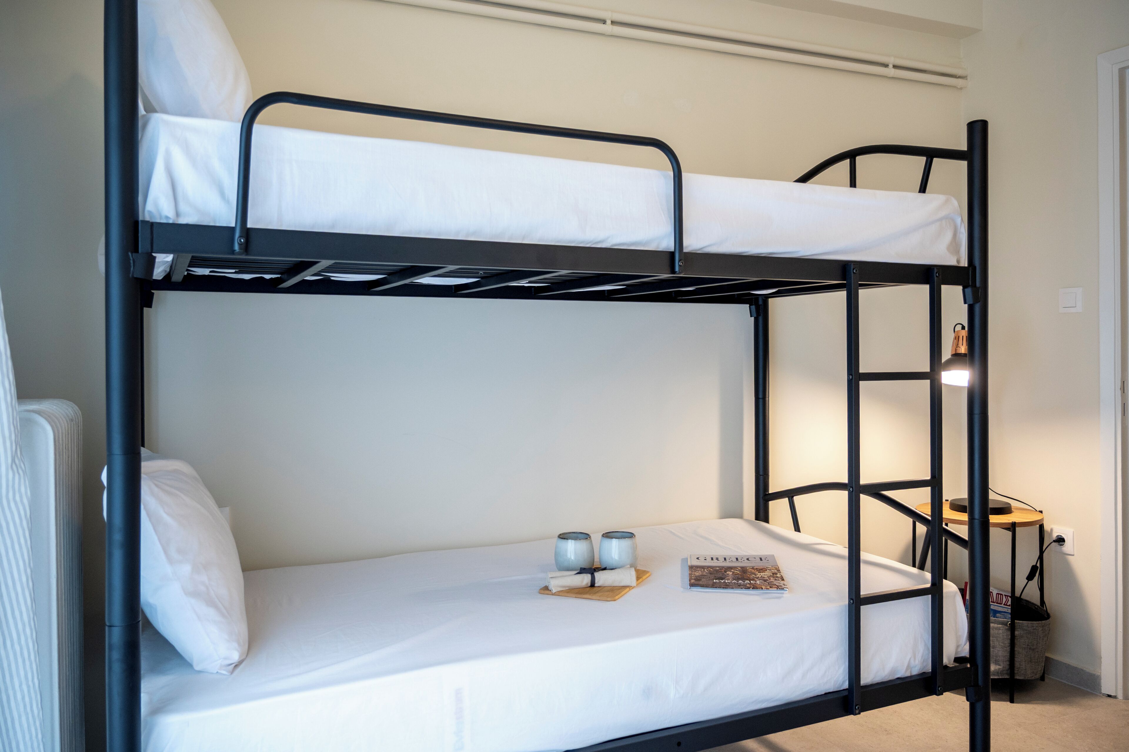 A bunk bed with a lower bunk, a bedside table with two cups, and a book on the lower bed.