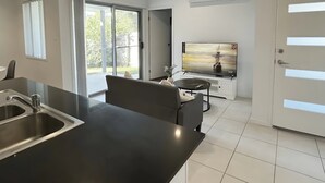 Una cucina moderna con un piano di lavoro nero, lavello in acciaio inossidabile e un grande televisore a schermo piatto montato a parete.