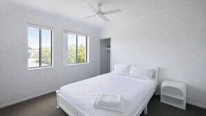 Una camera da letto con un letto, una ventola a soffitto e due finestre.