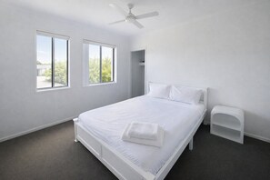 Ein Schlafzimmer mit einem Bett, einem Deckenventilator und zwei Fenstern.