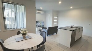 Una cucina moderna con un'isola centrale, una zona pranzo con tavolo e sedie rotonde, e un soggiorno con divano e televisore.