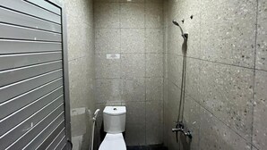 Une petite salle de bain carrelée, équipée de toilettes, d’une douche et d’un sèche-mains.