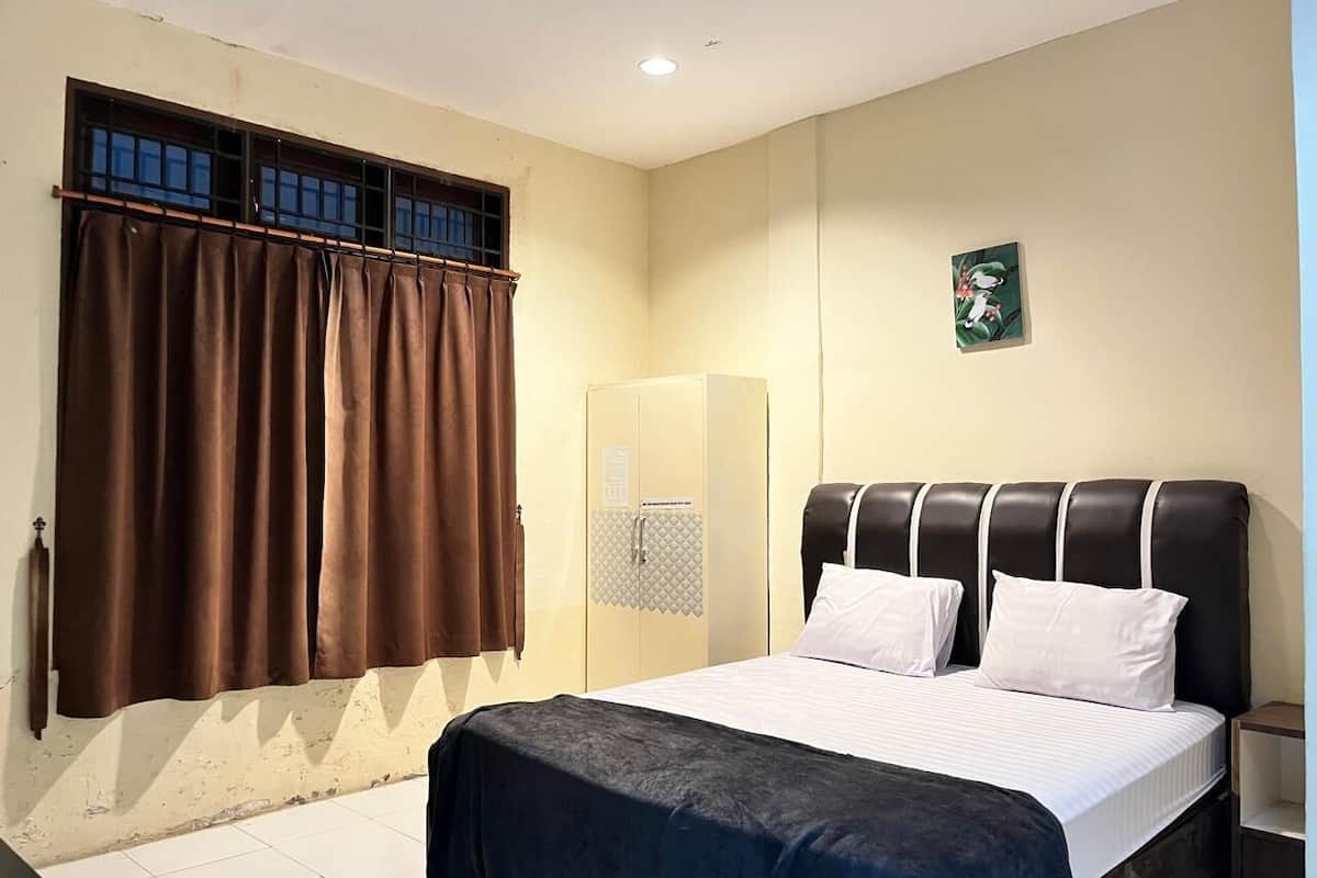 A bedroom with a bed, curtains, a wardrobe, and a small picture on the wall.