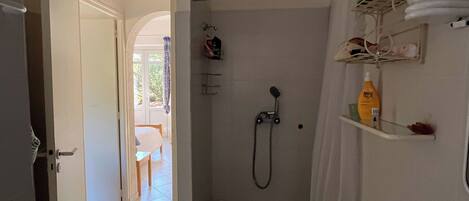 A bathroom with a shower, toilet, and sink. There is a door leading to a balcony.