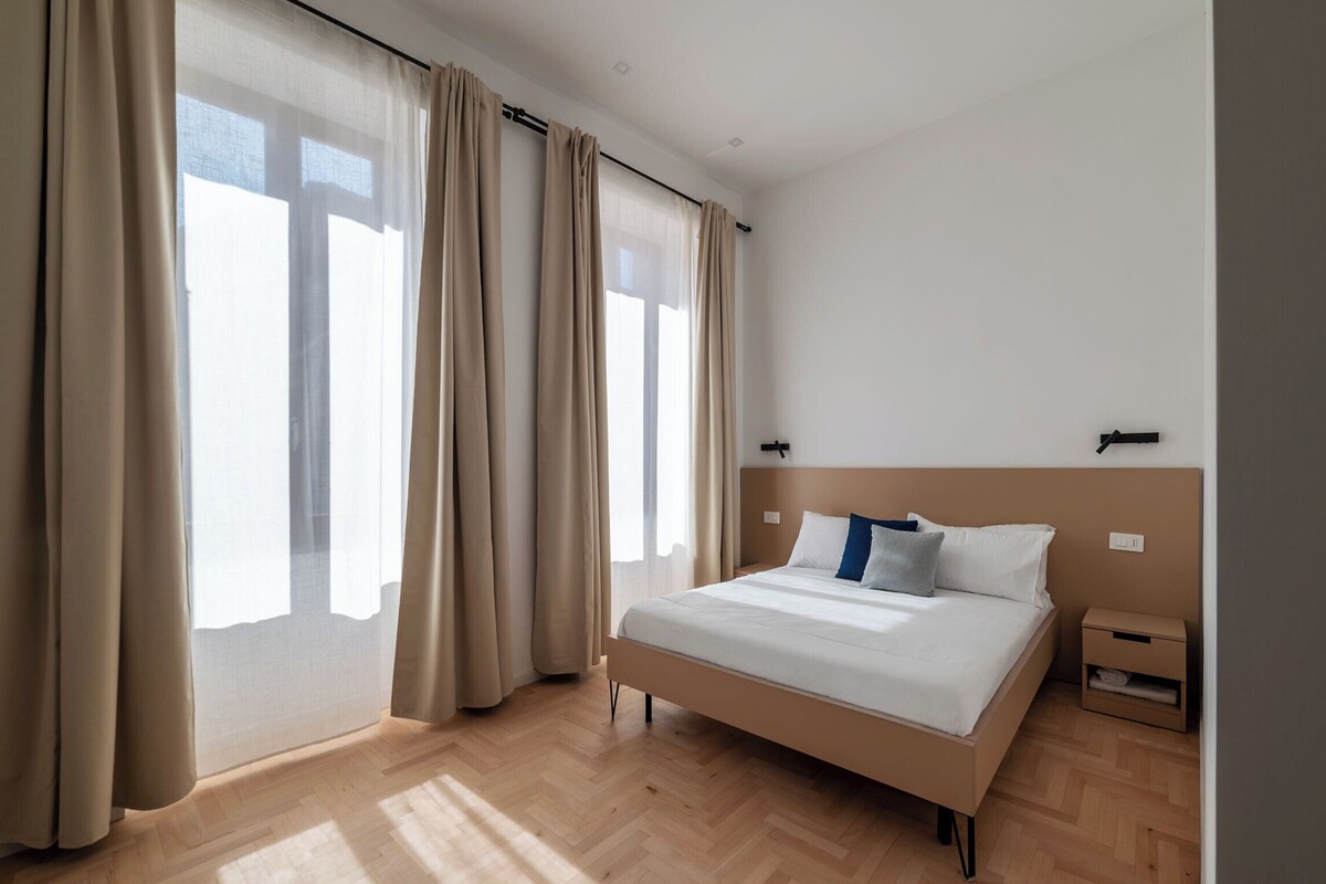 A bedroom with a bed, curtains, a nightstand, and a headboard.