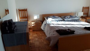 Ein Schlafzimmer mit einem hölzernen Bett, einem Nachttisch, einem Schreibtisch mit Stuhl und einem Spiegel.
