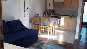Ein kompakter Wohnraum mit einem blauen Sofa, einem Esstisch und einer Küchenzeile.