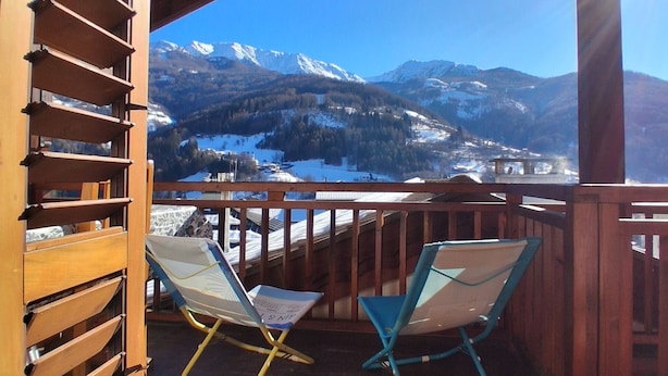 Ein Holzbalkon mit zwei Stühlen mit Blick auf eine verschneite Berglandschaft.