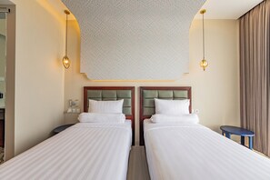 A hotel room with two beds, a small table, and a wall-mounted light fixture. - Azana Boutique Hotel Solo (Surakarta)