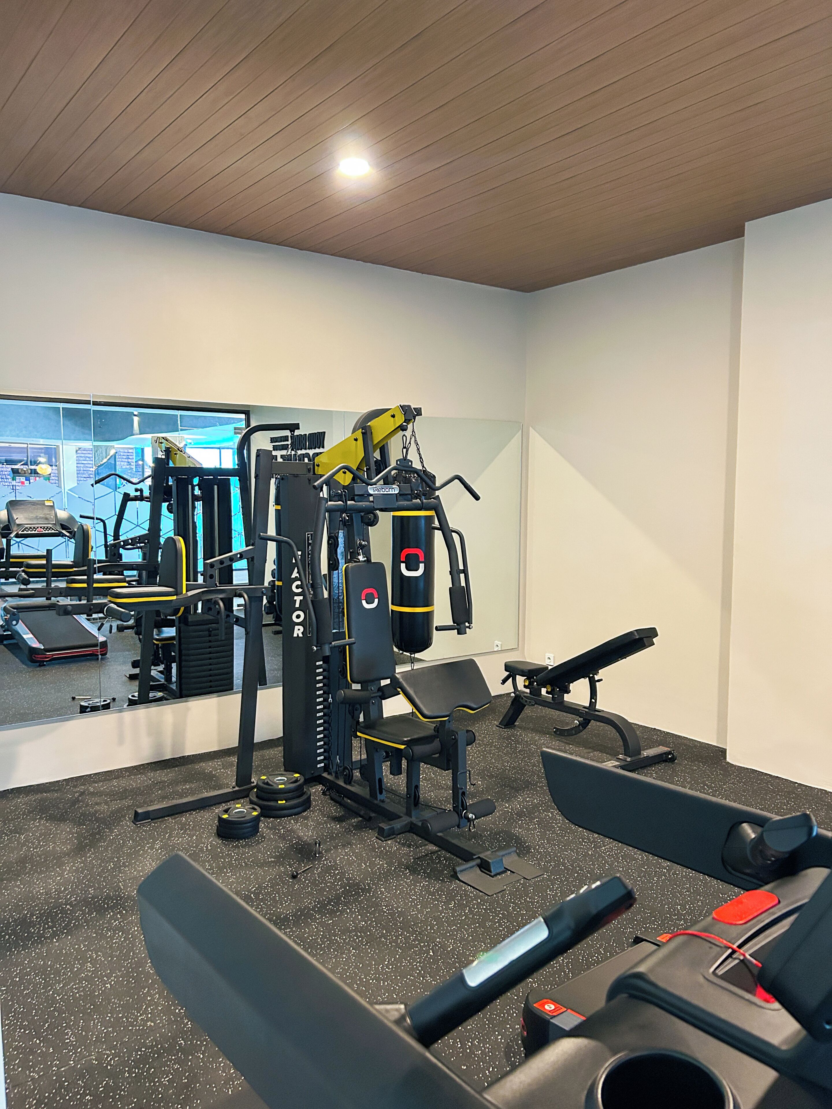 Un gimnasio con equipo de ejercicio, bancos y un espejo que refleja el espacio.