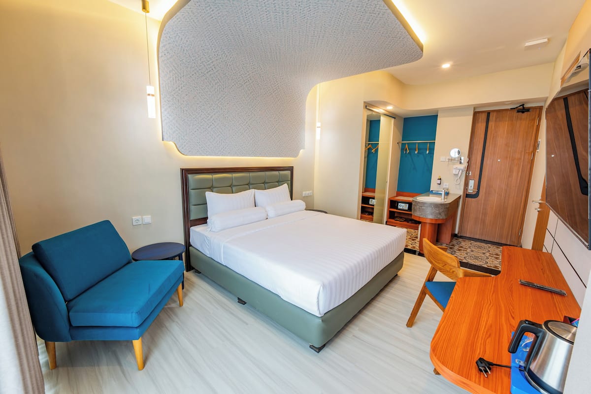 Une chambre d’hôtel avec un lit, un canapé bleu, une table en bois et un petit coin cuisine.