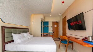 Une chambre d’hôtel avec un lit, un bureau, une chaise, une télévision et une salle de bain visible à travers une porte ouverte.