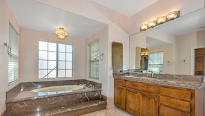 A bathroom with a large bathtub, wooden vanity, marble flooring, and a large mirror. - Peaceful spacious studio in Vista surrounded by greenery and birdsong. (Vista)