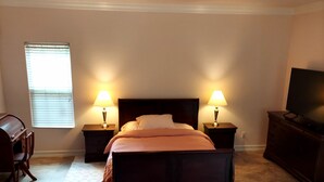 A bedroom with a bed, two bedside lamps, a TV on a dresser, a desk, and a window with blinds. - Peaceful spacious studio in Vista surrounded by greenery and birdsong. (Vista)