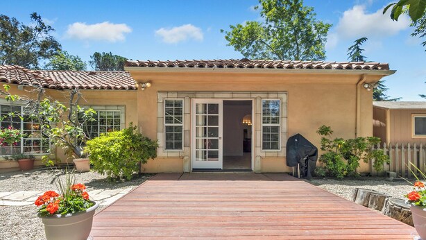 A house with a wooden deck leading to a glass door entrance, surrounded by potted plants and a picket fence. - Peaceful spacious studio in Vista surrounded by greenery and birdsong. (Vista)