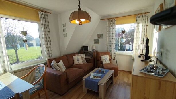A cozy living room with a brown sofa, a coffee table, and a dining area with a table and chairs. - FeWo Fokko - Away from the hustle and bustle (Norden)
