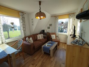 A cozy living room with a brown sofa, a coffee table, and a dining area with a table and chairs. - Fokko Vacation Rental - A peaceful retreat away from the hustle and bustle (Norden)