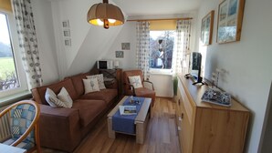 A cozy living room with a brown sofa, a wooden coffee table, and a TV on a wooden cabinet. - FeWo Fokko - Away from the hustle and bustle (Norden)