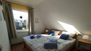 A bedroom with a large bed, a window with curtains, a bedside table with a lamp, and a radiator. - FeWo Fokko - Away from the hustle and bustle (Norden)