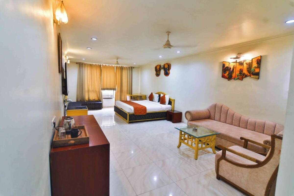 A hotel room with a bed, a sofa, a coffee table, and a desk with a lamp.